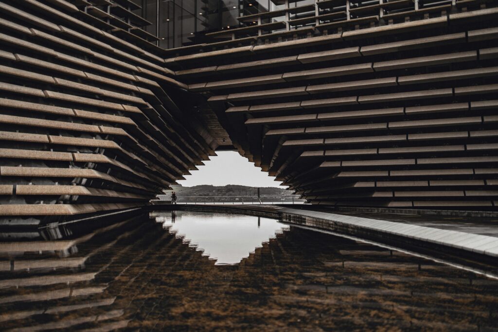 The angular geometric facade of a modern architectural building reflected in a pool of water