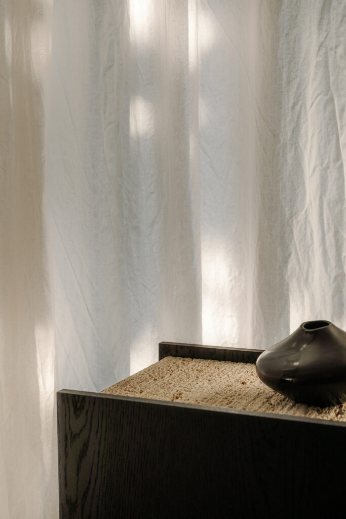 A minimalist Japanese interior with soft light filtering through white fabric, a sand-filled shelf, and a dark ceramic vase