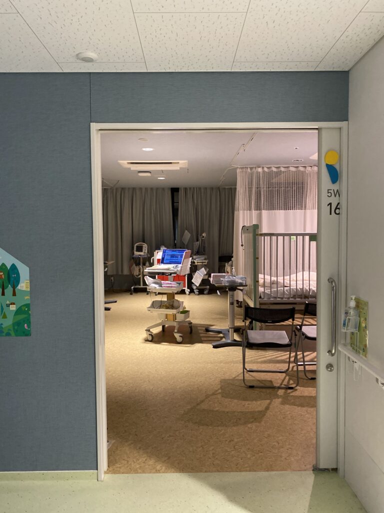 A children's hospital room in Japan viewed through an open door, with medical equipment and colourful wall murals